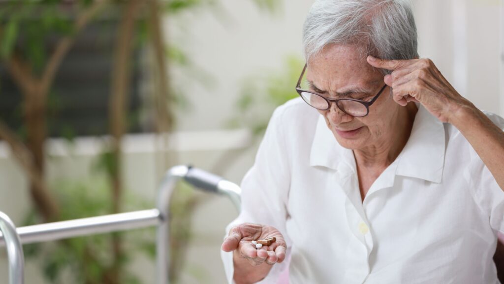 A older lady appears in mild distress as she looks at a collection of tablets in her hand. For thos people living with memory chalenges, medication can be a source of distress and potential danger. A live-in carer can and will help keep you or a love one safe and worry free by helping with medication.