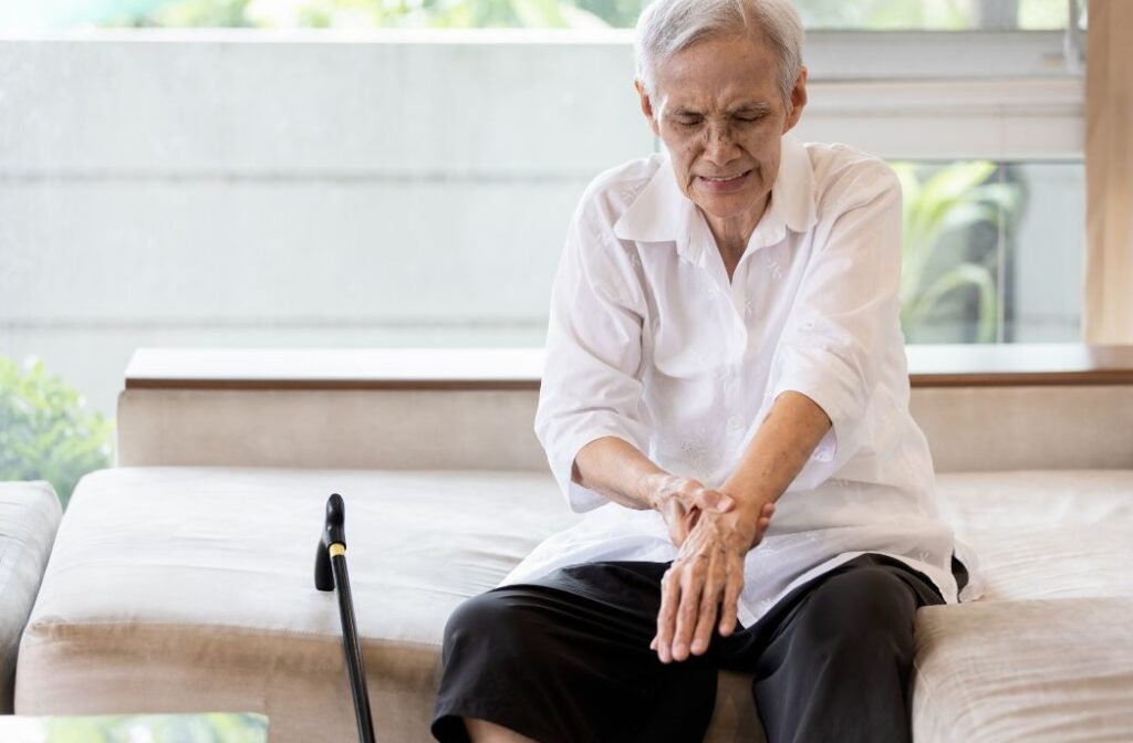 An older adult clutches at their left wrist which has been affected by a stroke. By moving and working the arm, joitns and muscles the brain is able to relearn control through a process called neuoplasticity. A live-in carer can and will help with exercise that keep you fit and independent, happy in your own home, hopefully forever.