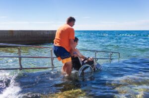 man helping young adult with disability have fun on holiday on the beach