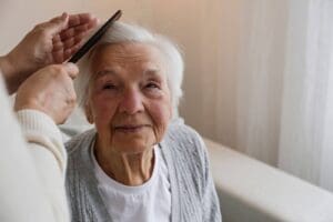 A professional home care worker brushing an elderly client’s hair.