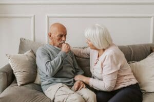 Man in grey jumper sitting on couch with concerned looking woman