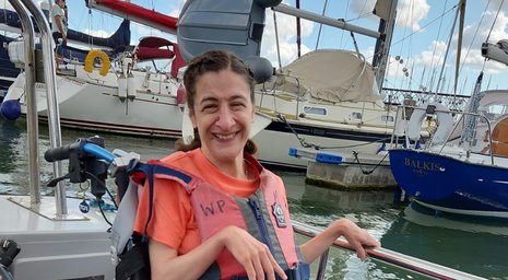 Young woman in a wheelchair smiling aboard a boat in a busy marina during a complex live-in care outing.