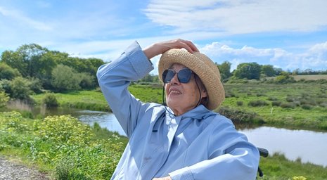 Older woman in a wheelchair enjoying a sunny riverside outing during live-in care support
