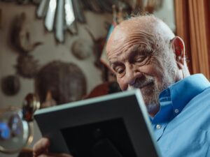 An elderly man in a blue shirt looking at photograph in lounge 