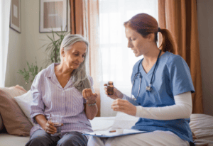A nurse sits on a bed beside an older woman, providing care and support in a warm, comforting environment