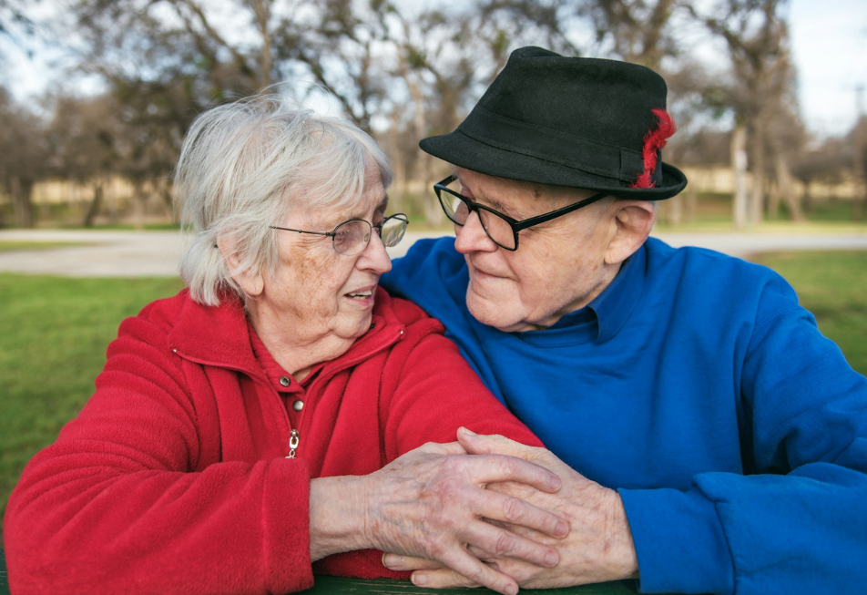 Elderly couple sitting together outside, holding hands and smiling — conveying comfort, companionship and family decision‑making in care.