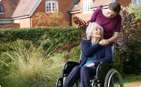 A woman in a wheelchair smiles while conversing with an older woman, both engaged in a friendly discussion.