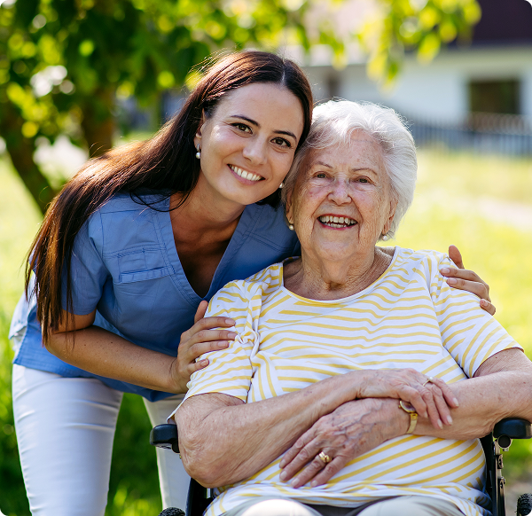 A woman in a wheelchair smiles while conversing with an elderly woman, both enjoying a sunny outdoor setting.