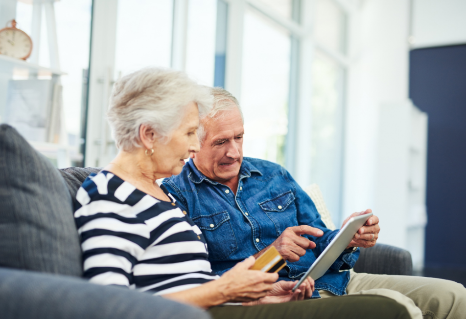 An older couple sits together on a couch, engaged in viewing content on a tablet device