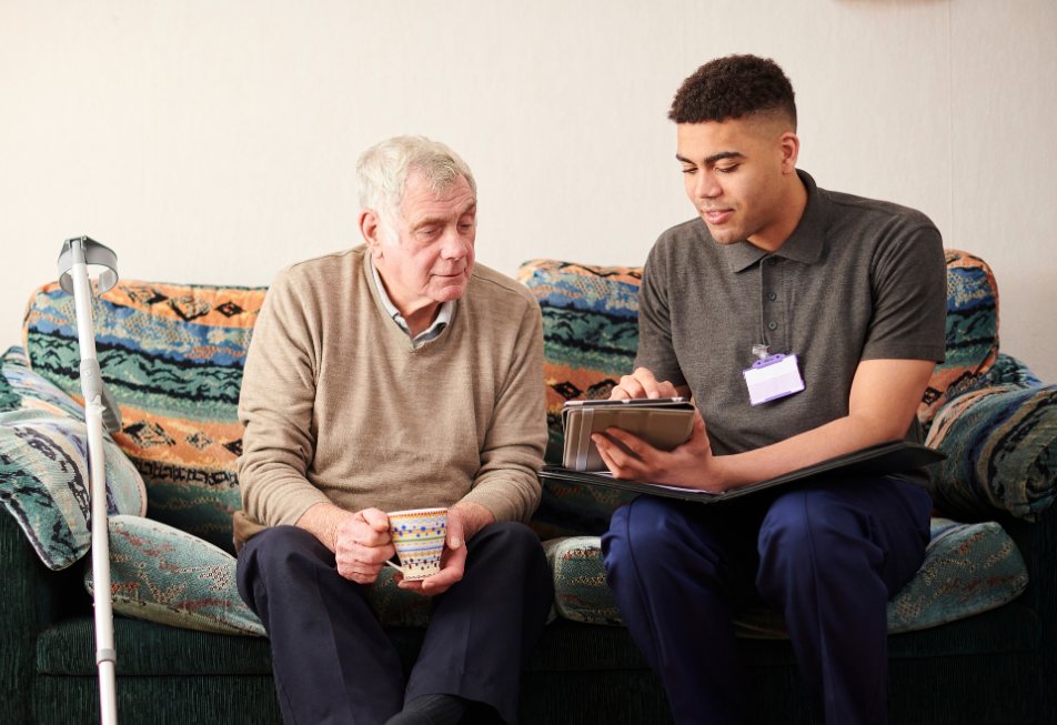 A man sitting on a couch, holding a cane, appears relaxed and contemplative in a cozy living room setting
