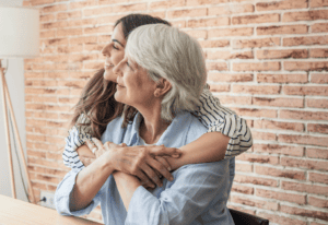A woman embraces her mother while seated at a table, conveying warmth and affection between them