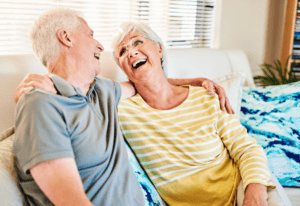 An older couple joyfully laughing together while sitting on a cozy couch