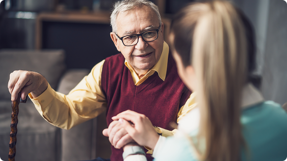 A man with glasses and a cane converses with a woman in a casual setting.