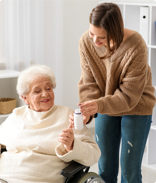 A woman in a wheelchair hands a bottle of medicine to an elderly woman, showcasing care and support between them