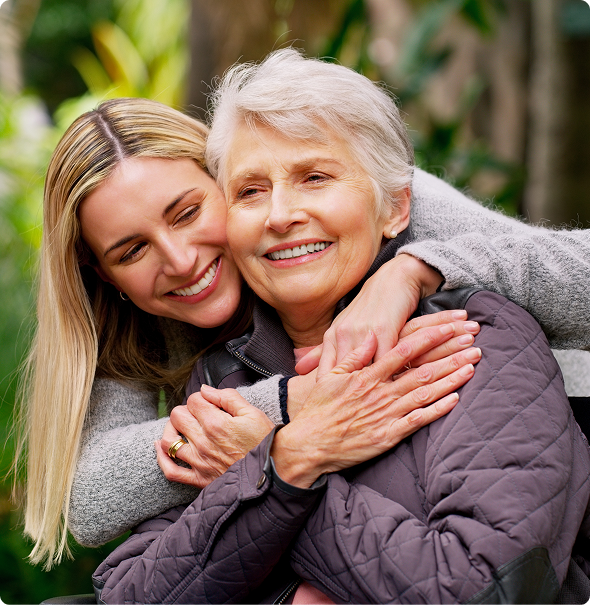 A woman embraces an older woman in a wheelchair, conveying warmth and support in a heartfelt moment.