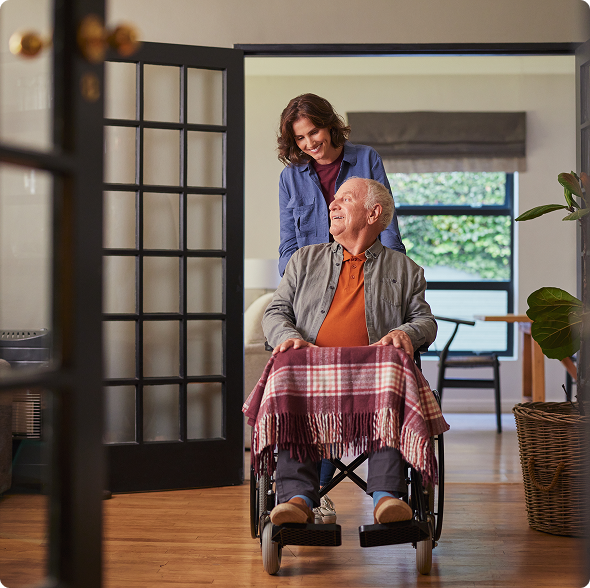 A woman assists an elderly man in a wheelchair, providing support and guidance in a caring manner