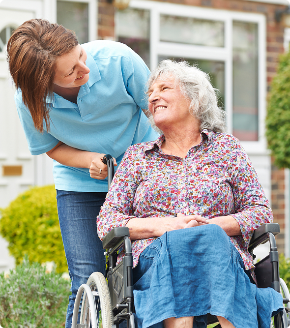 A woman in a wheelchair smiles alongside another woman wearing a blue shirt, both engaged in conversation.
