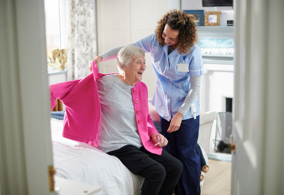 A woman assists an older woman in putting on a jacket, showcasing a moment of care and support between them