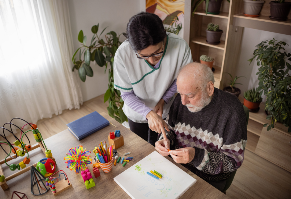 A woman assists an elderly man as he works on his craft project, showcasing collaboration and support in their activity