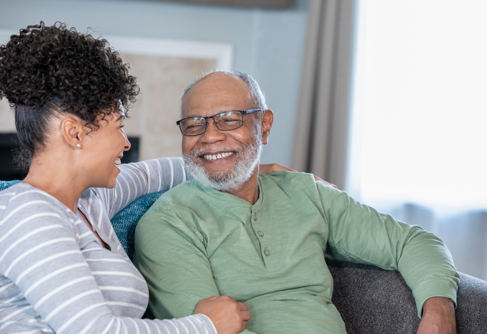 A smiling black man and woman sit together on a couch, exuding warmth and happiness in a cozy living room setting