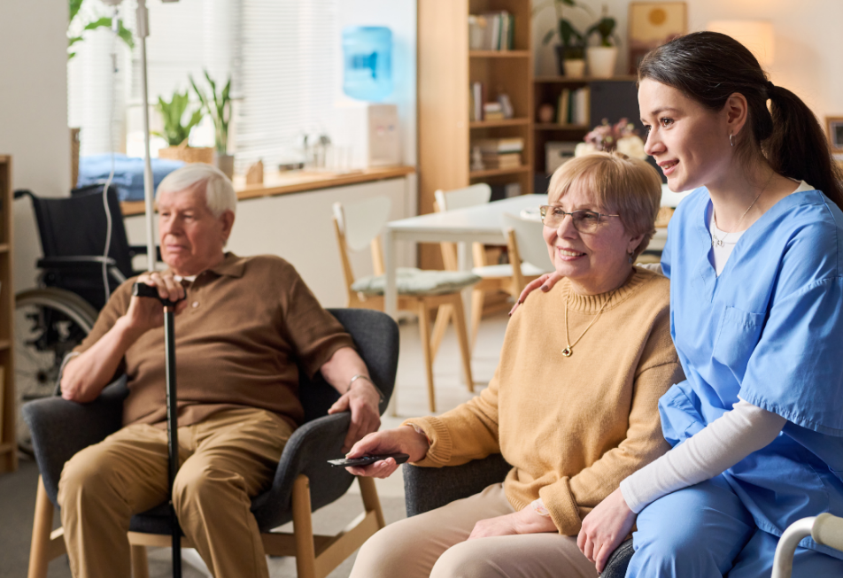 A nurse assists two elderly individuals seated in chairs, fostering a supportive and caring environment
